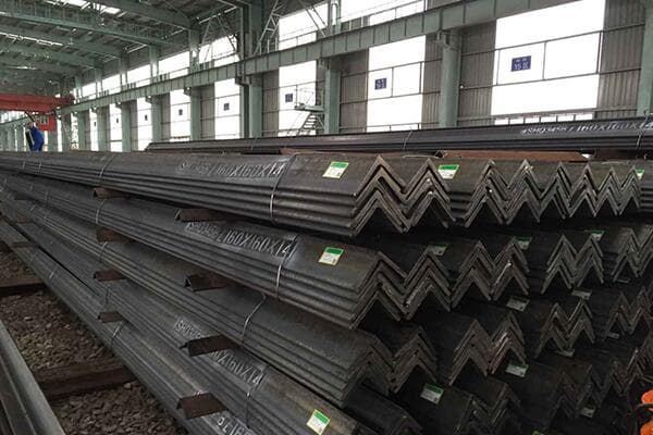 Neatly organized stacks of L-shaped steel angle bars inside a large industrial factory setting.